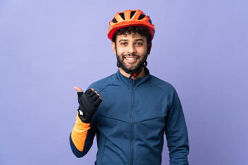 Young Moroccan cyclist man isolated on purple background pointing to the side to present a product