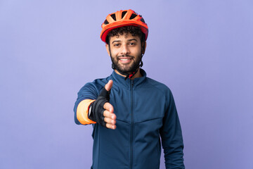 Young Moroccan cyclist man isolated on purple background shaking hands for closing a good deal