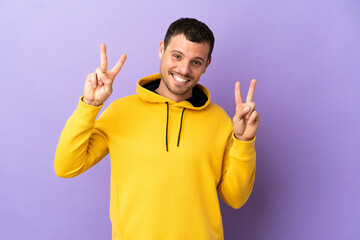 Brazilian man over isolated purple background showing victory sign with both hands