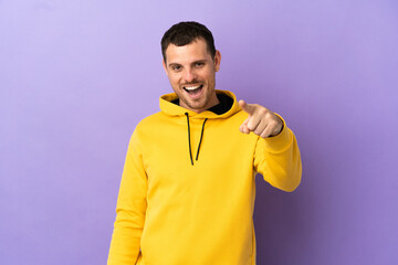 Brazilian man over isolated purple background surprised and pointing front