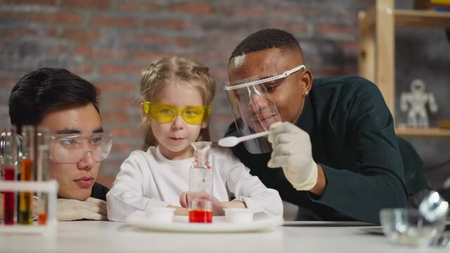 Little girl student adjusts funnel and stirs material in lab