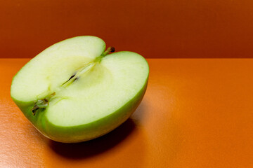 Half of a green apple on an orange background. Sliced apple on the table