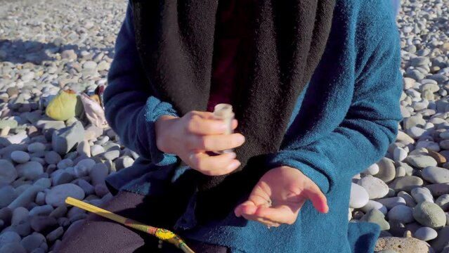 woman pours powder on palm of her hand, wooden tray with Peruvian sacred palo Santo tree, feathers other attributes of rape on pebble beach.Esoteric objects for meditation. Antistress and relaxation