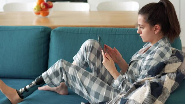 Serious woman with artificial bionic high technology leg prosthesis texting by tablet at home