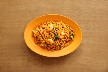 Mie Goreng in an orange bowl on a wooden table background top view Chinese food. (Indonesian cuisine). Fried noodles with prawns
