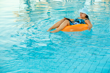 A woman in a swimsuit and a sun hat in the pool in a swimming circle with a laptop and a cocktail in her hands.
