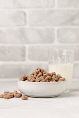 Bowl with chocolate corn or oat rings and a glass of milk on light table. Whole grain breakfast cereals with copy space