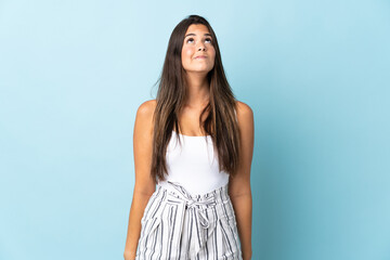 Young brazilian woman isolated on blue background and looking up