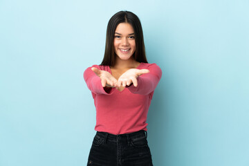 Teenager girl isolated on blue background holding copyspace imaginary on the palm to insert an ad