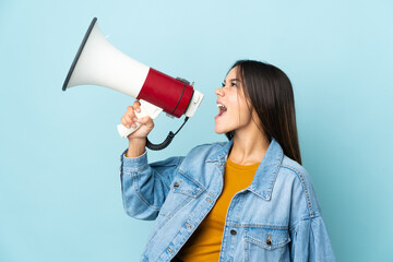 Teenager girl isolated on yellow background shouting through a megaphone to announce something in...