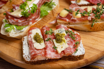 Delicious appetizer bruschetta with bacon, blue cheese, herbs and prosciutto on table, close-up