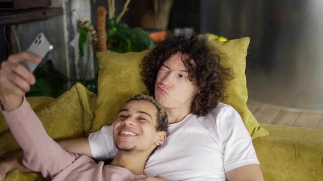 Male romantic gay couple relaxing on the couch, taking selfie with smartphone, posing