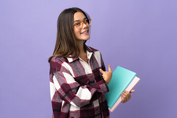 Fototapeta premium Young student woman isolated on purple background pointing back