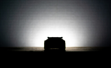 front silhouette of a sports car being illuminated against a white background 