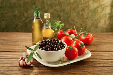 Mesa de madeira com tigela com tomates, azeitonas pretas e frascos de azeite extra-virgem © Pic_It