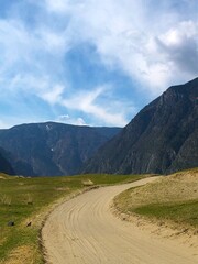 A road without asphalt, a primer among the mountains in spring and a blue sky with clouds