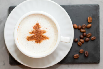white cup of coffee cappuccino on a concrete background next to coffee beans