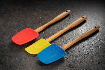 Silicone kitchen spatulas in blue, red and yellow colors on a black surface.