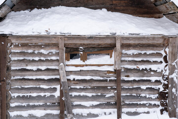 The wall of a small old wooden bathhouse in winter. Snow stuck between the logs of the wall and at the window. Background. Village architecture.