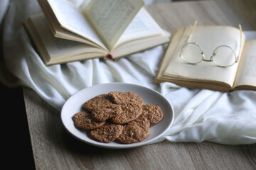 Plate of healthy gluten free cookies, open books and reading glasses on the table. Selective focus.
