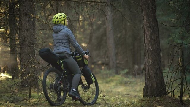 The woman travel on mixed terrain cycle touring with bike bikepacking. The traveler journey with bicycle bags. Magic forest park.
