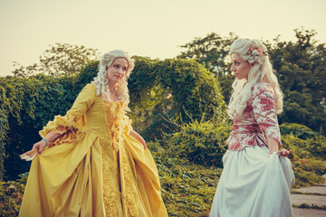 Fototapeta premium Portrait of two blonde woman dressed in historical Baroque clothes with old fashion hairstyle, outdoors. Luxurious medieval dress