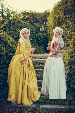 Portrait of two blonde woman dressed in historical Baroque clothes with old fashion hairstyle, outdoors. Luxurious medieval dress