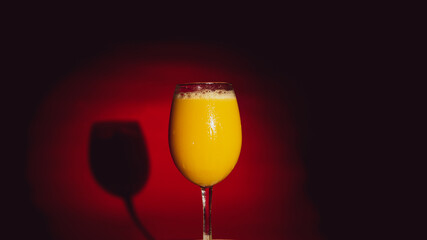 Glass of cool juice stands out on red background in shading. Healthy fresh juice highlighted in shadow.