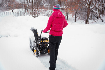 A woman clears the road from snow with a snow blower.
