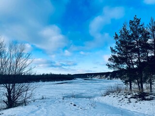 Winter landscape of snow-covered river between forests. Beautiful scenery of frozen river on cloudy...