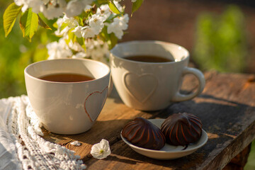 Coffee with milk, cocoa, tea in cups with heart decor, lace napkin on a wooden table. Cherry blossoming branches, spring mood. Outdoor brunch refreshments.