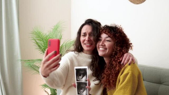 LGBT lesbian couple holding ultrasound photo scan on video call of growing baby in pregnancy time