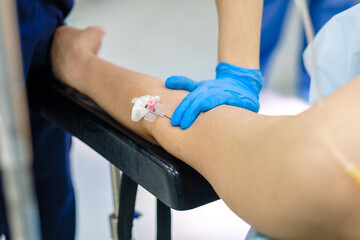 Dropper needle in a vein on the patient's arm, lying on the operating table. Selective focus. Intravenous drug administration through a catheter.
