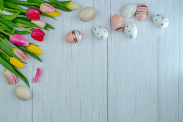 Bouquet of multicolored fresh tulips and decorative Easter eggs on pink marble. The concept with copy space is suitable for the design of a greeting card, banner, calendar.