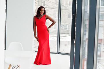 Fototapeta na wymiar Magnificent young african woman in luxurious red dress in a luxury apartment. Beauty, fashion.