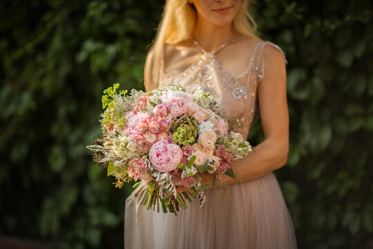 Portrait of an elegant unrecognizable pretty woman wearing grey wedding dress and posing in the street. Bride holds a bouquet of pastel flowers and greenery