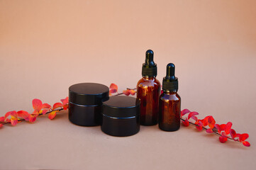 Brown cosmetic bottles on a beige background with red-orange-pink autumn branches of the spirea tree. The basis for inspiration in cosmetic products. Cosmetic background for product presentation.