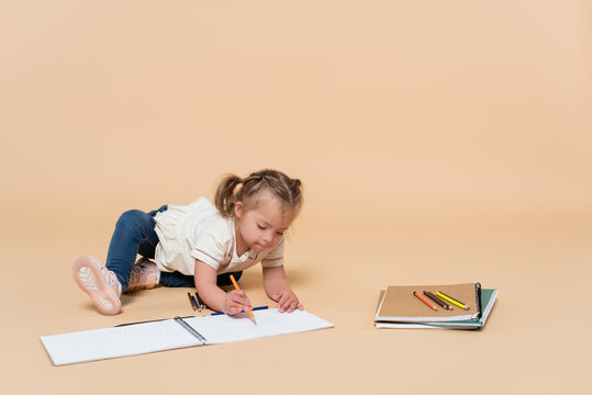 girl with down syndrome drawing near colorful pencils and backpack on beige.