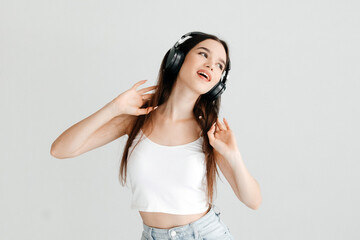 Brunette woman listening to music in wireless headphones singing, looking to the side, on white background