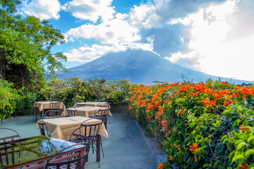 tables on an outdoor terrace overlooking the mountainous natural landscape, a cloudy sky and a volcano.