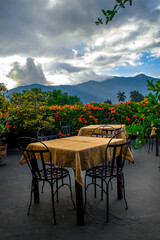 tables on an outdoor terrace overlooking the mountainous natural landscape, a cloudy sky and a volcano.