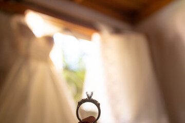 wedding ring seen up close, with the dress and veil in the background, in the bride's room lit by light from the window at sunset.
