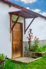 Entrance door, rustic wood and tin roof of a country house with a garden around it, under a blue sky.