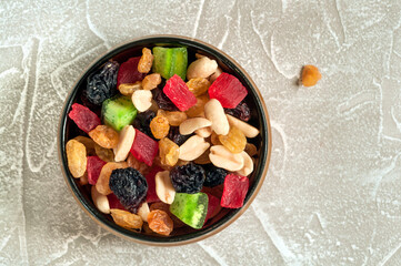 Mix of nuts and dried fruits in a round bowl on a gray marble background. Top view, close-up with natural light