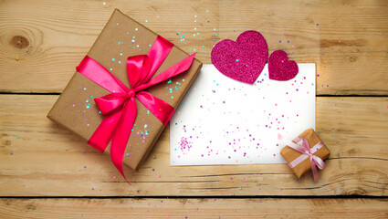 Top view photo of Valentine's day decor gift box, paper heart,sequins and a sheet of paper on a wooden background.