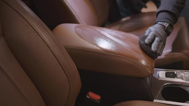 Closeup of hand of worker wipe and polish leather armrest. Professional detailing worker applies protective coating. Carwash or Car Detailing process