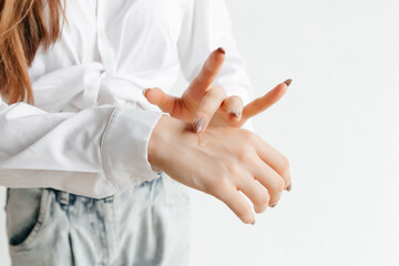 Fototapeta premium Woman in white shirt spreading hand cream over her hand. Close up. cold season hands skin protection. closeup woman applying protective cream on hands.