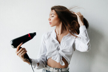 Sexy young woman drying her straight long brunette hair with closed eyes on white background. Woman is getting ready for going out