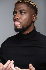 serious african american man with vitiligo gesturing and looking away while thinking isolated on grey.