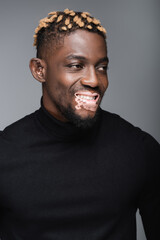 Fototapeta premium happy african american man with vitiligo and trendy hairstyle looking away isolated on grey.